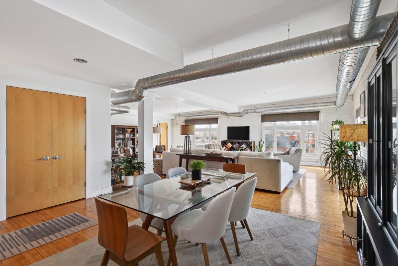 Open-concept dining and living area with exposed ductwork, white-painted brick and hardwood floors