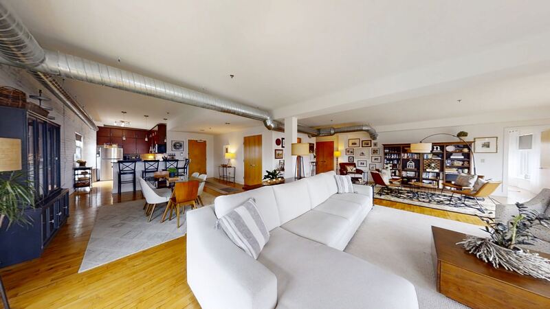 Inside a two-bedroom: an open living and dining room under exposed ductwork, with the kitchen beyond